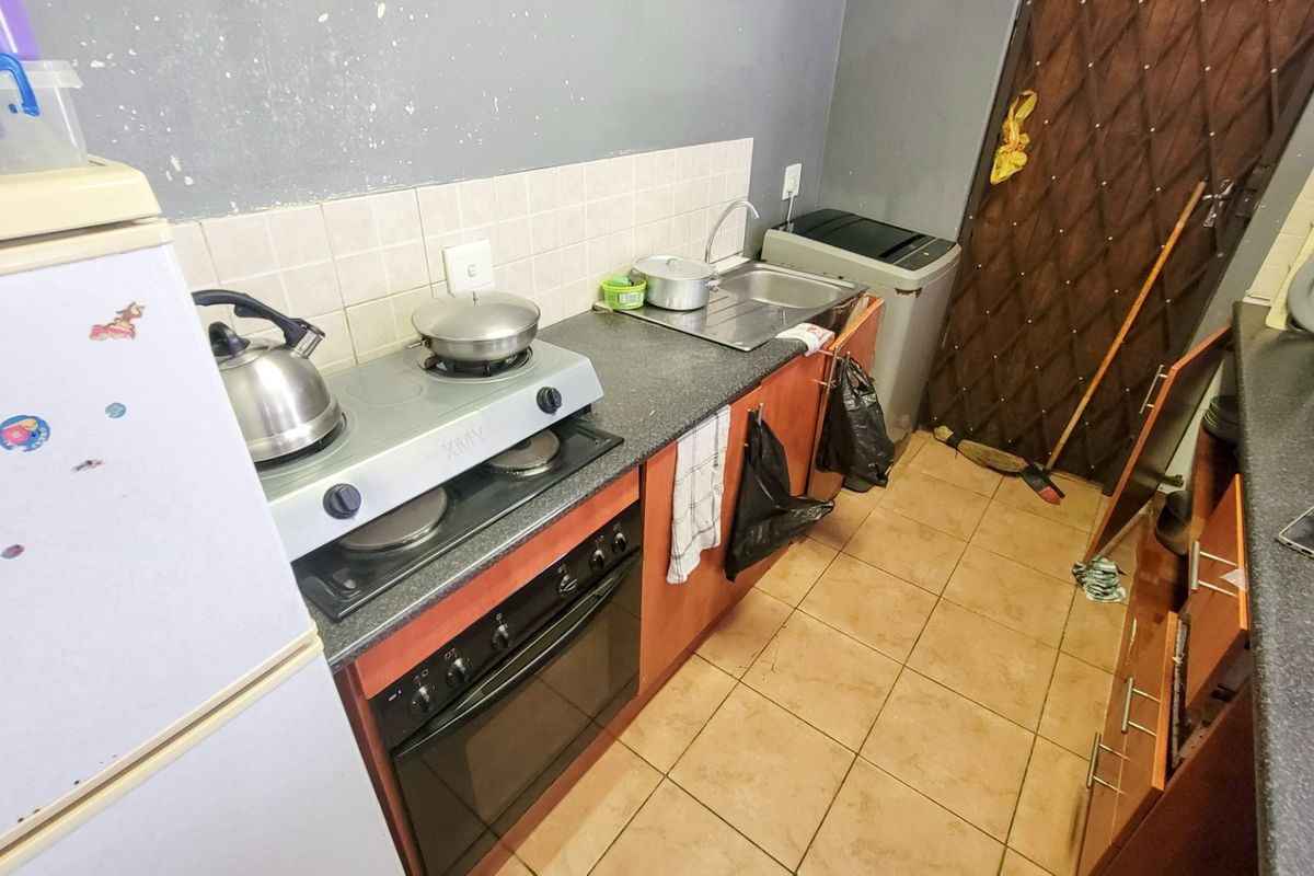 A compact kitchen featuring a gas hob, built-in oven, stainless steel sink, and tiled splashback with laminate cabinetry and tiled flooring.