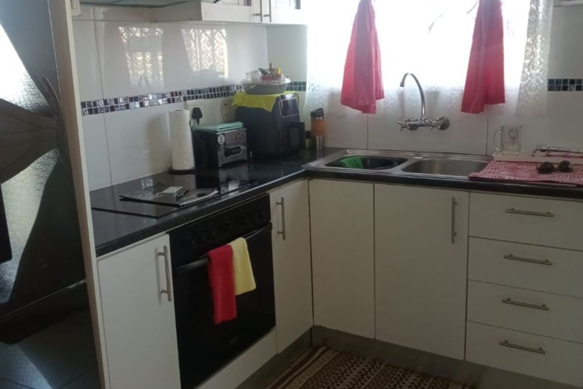 A compact kitchen featuring white cabinetry, dark countertops, a built-in oven with hob, extractor fan, and a double sink with tiled splashback.