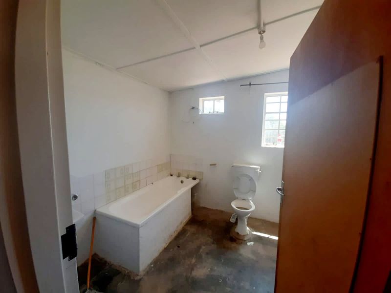 A basic, unfinished bathroom featuring a standard bathtub and toilet, requiring significant renovation and flooring installation to complete the space.