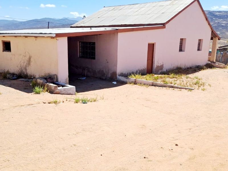 Rear view of a detached house featuring a covered patio area, corrugated metal roofing, and masonry construction in need of exterior maintenance.