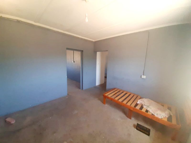 A sparsely furnished bedroom featuring grey painted walls, exposed surface wiring, and basic flooring, offering a blank canvas for renovation.