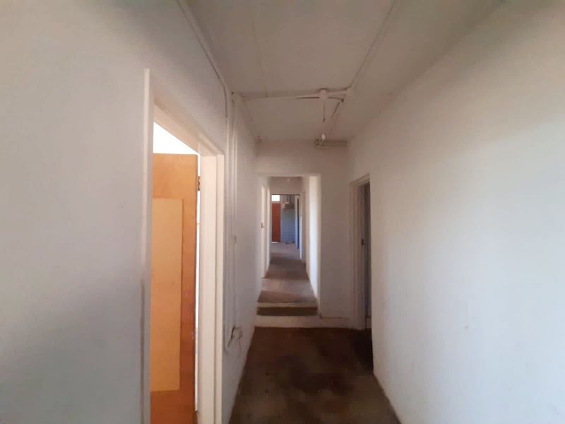 A long, empty hallway featuring exposed electrical conduit and worn flooring, providing access to multiple rooms within the property.