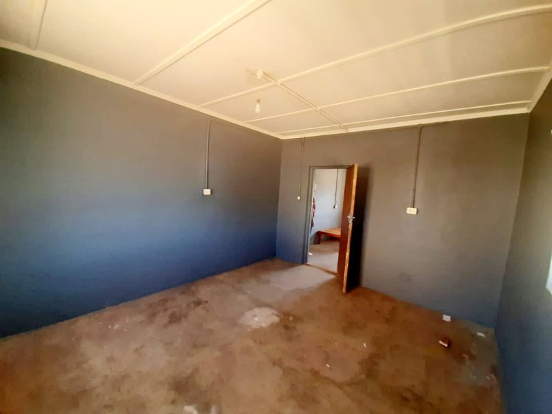 An empty bedroom featuring dark painted walls, exposed electrical conduit, and worn flooring, offering a blank canvas for renovation.