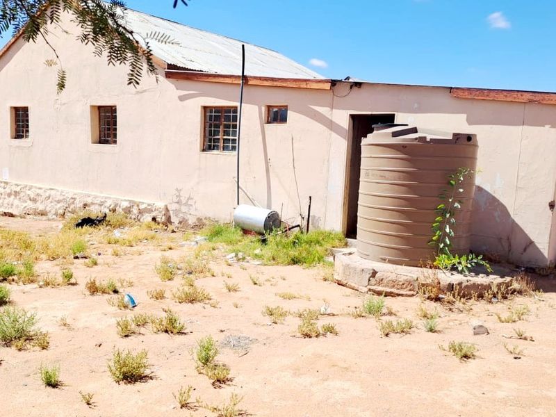 Rear view of the property featuring a water storage tank, stone base detailing, and a corrugated metal roof in need of maintenance.