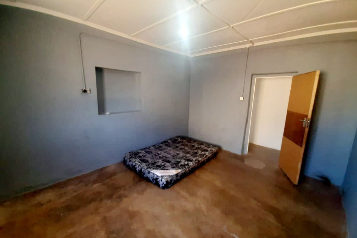 A sparse bedroom featuring grey painted walls, a recessed wall niche, and exposed electrical conduit, providing a blank canvas for renovation.