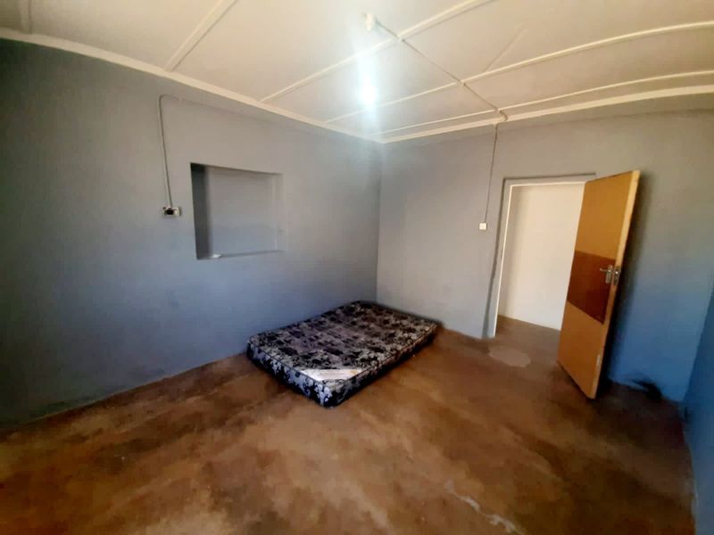 A sparse bedroom featuring grey painted walls, a recessed wall niche, and exposed electrical conduit, providing a blank canvas for renovation.