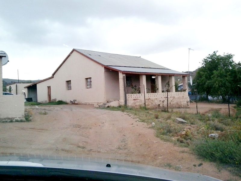 A single-story detached house featuring a covered front porch, corrugated metal roofing, and a large unpaved yard area.