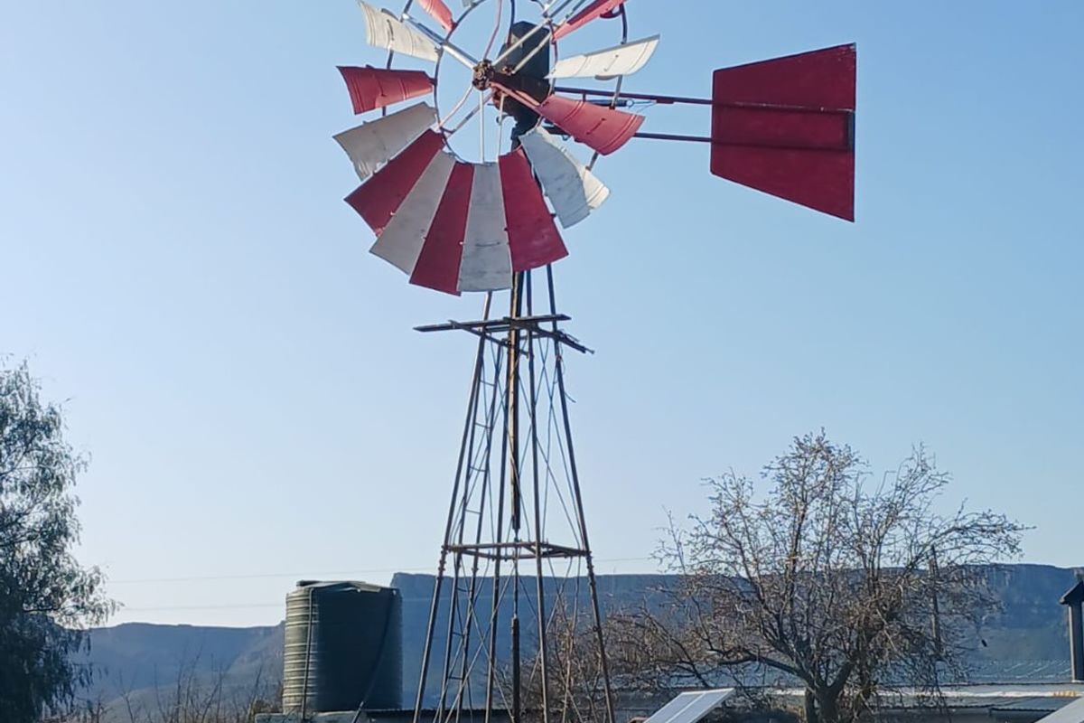 A farm property featuring a traditional windmill, water storage tank, and solar panel installation set against a rural landscape.
