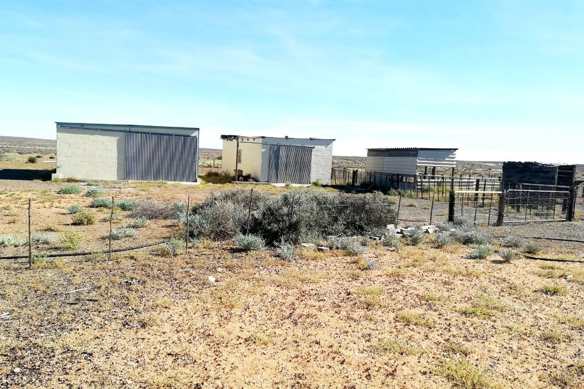 A view of multiple farm outbuildings featuring corrugated metal and concrete block construction, set within a rural landscape with wire fencing.