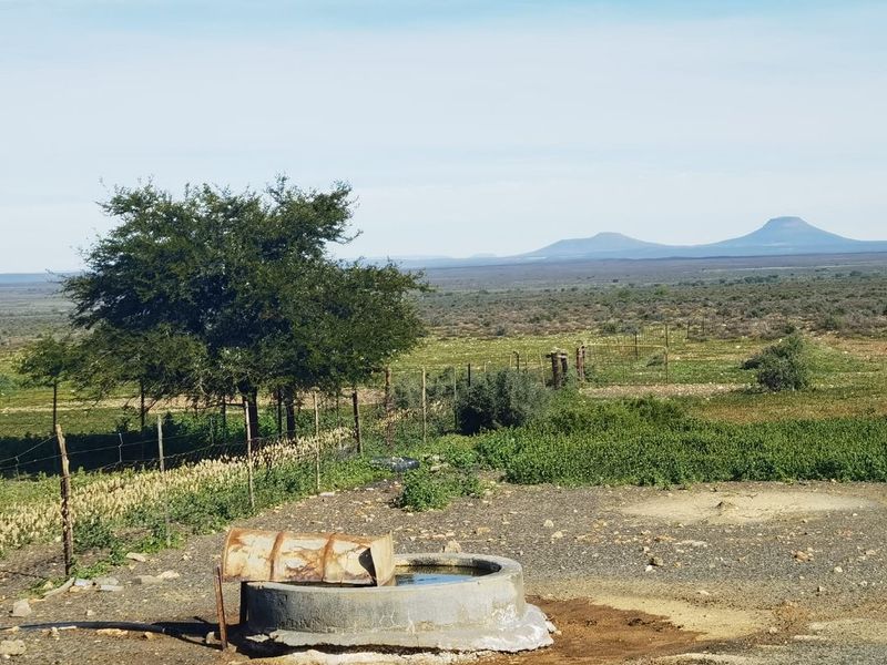 A wide landscape view of the farm property featuring open fields, wire fencing, and a concrete water trough in the foreground.