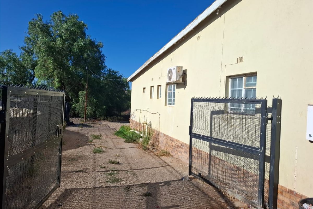 Rear exterior view of the commercial property featuring a security gate, perimeter fencing, and an external air conditioning unit mounted on the wall.