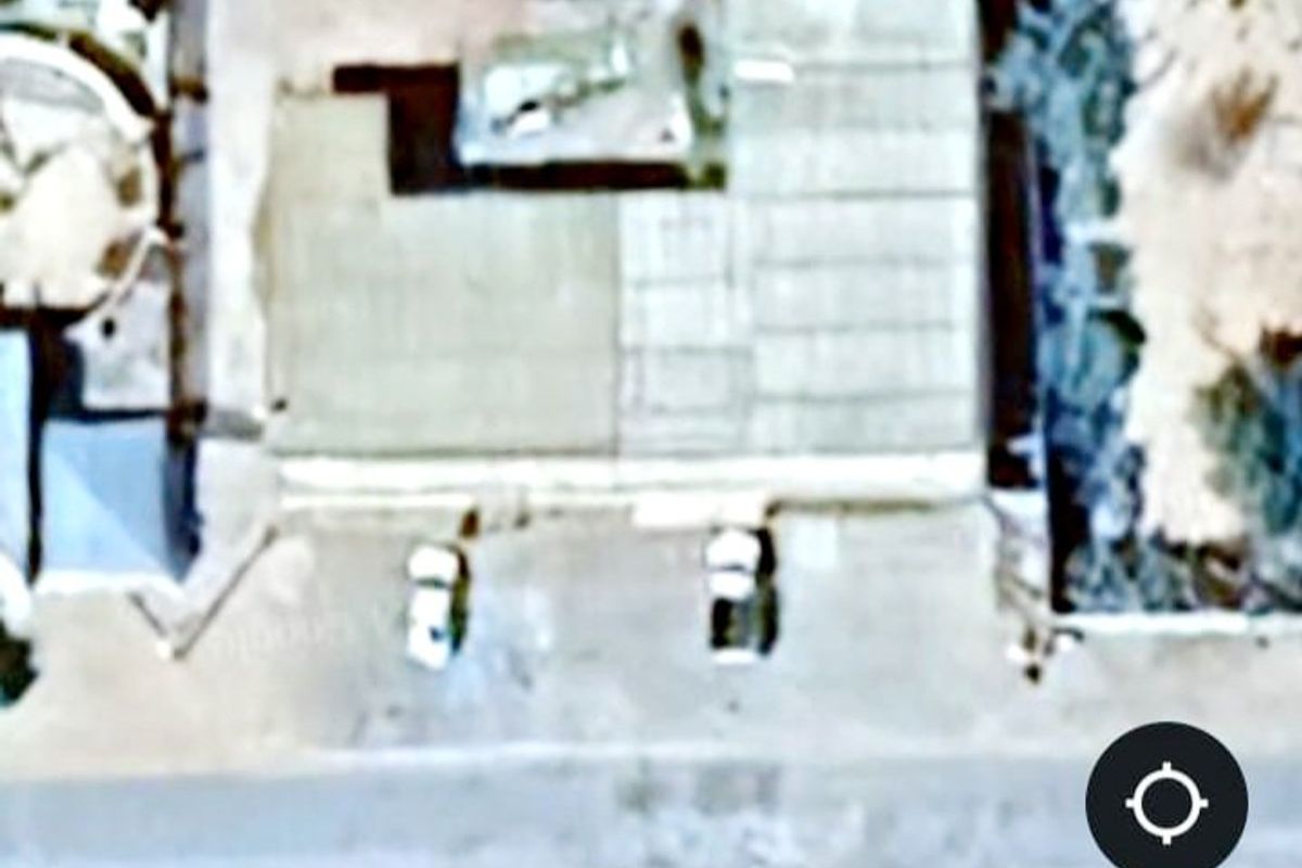 An aerial satellite view of the commercial property showing the building footprint, roof structure, and surrounding paved driveway area.