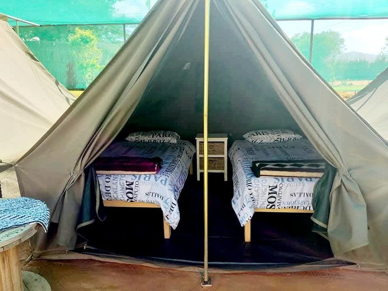 A canvas tent bedroom setup featuring twin beds under a protective shade netting structure, suitable for farm-style glamping accommodation.