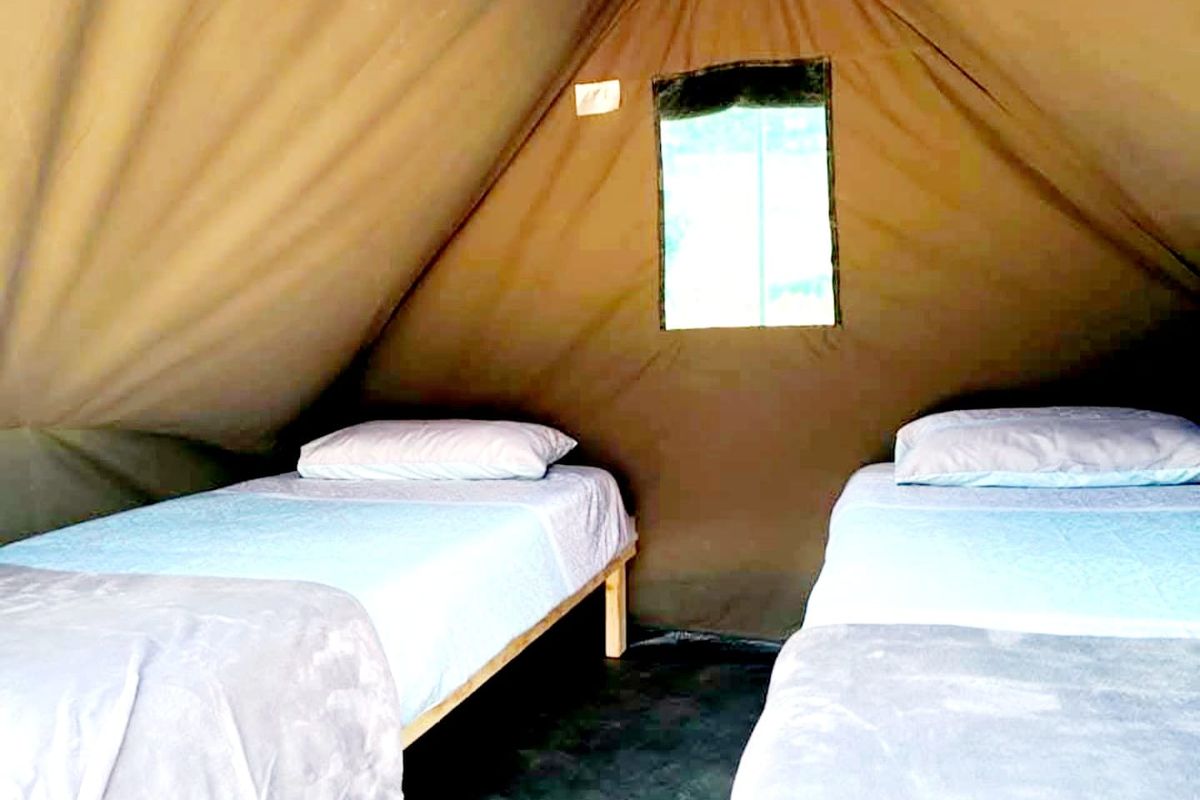 A rustic bedroom space within a canvas tent structure featuring a simple window and twin sleeping arrangements.
