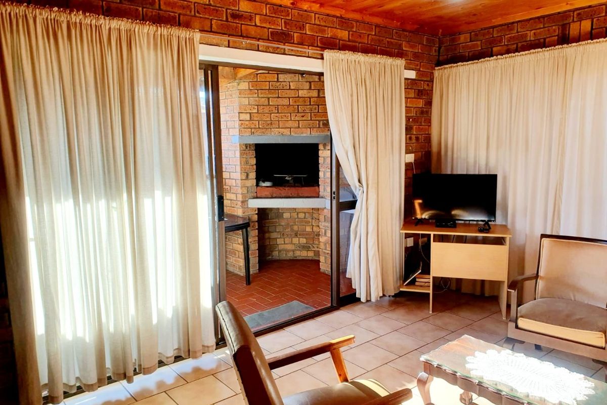 Living area featuring exposed brick walls, timber ceiling, and tiled flooring, with direct access to an outdoor patio area containing a built-in brick braai.