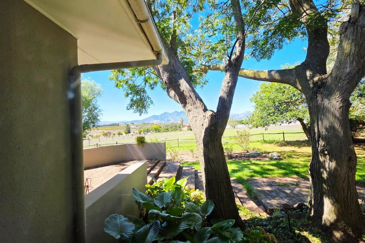 A rear exterior view featuring a brick paved patio, retaining wall, and expansive views of the surrounding farm landscape and distant mountains.