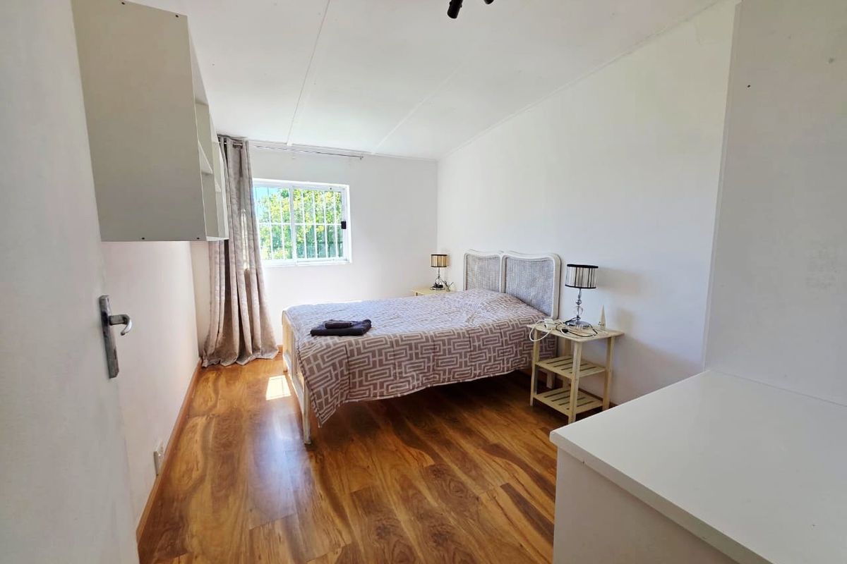 A functional bedroom featuring laminate flooring, built-in shelving, and a window fitted with security bars, offering a clean and simple living space.