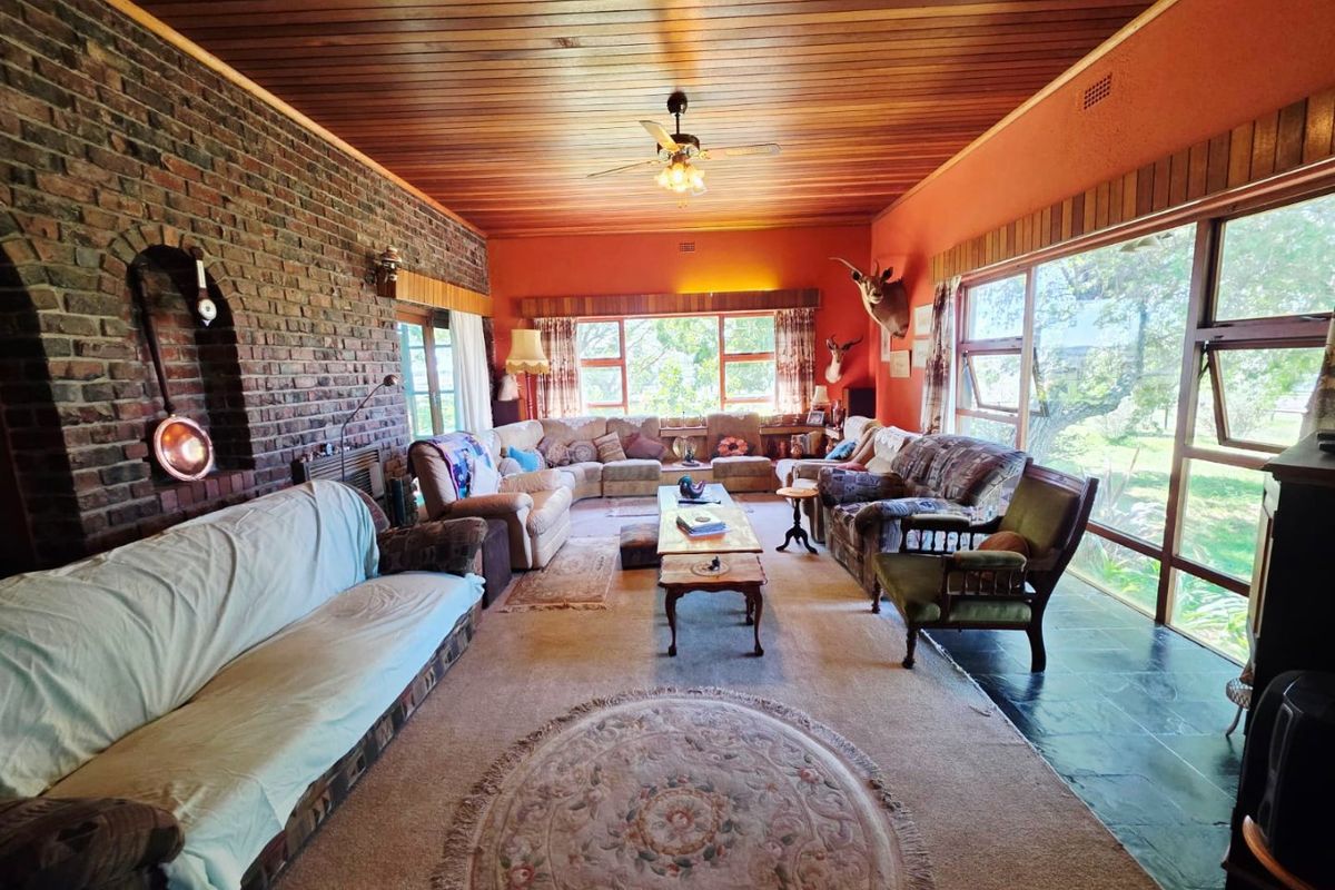 Spacious living room featuring an exposed brick feature wall, timber ceiling, and large windows providing natural light and garden views.