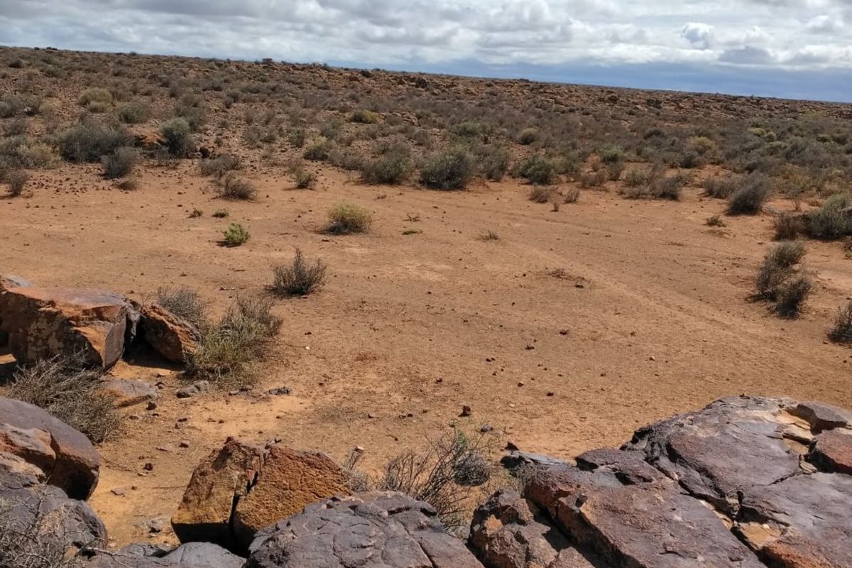 A wide-angle view of the expansive arid farm landscape featuring natural rock formations and native scrub vegetation under a cloudy sky.
