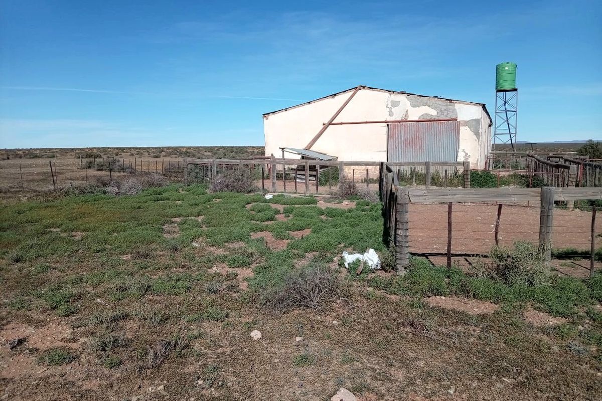 Exterior view of a farm outbuilding featuring a water tank, timber fencing, and weathered wall finishes in a rural landscape setting.