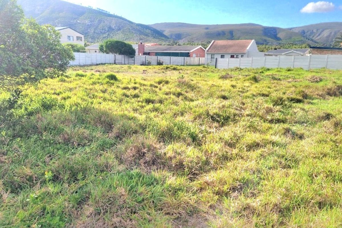 A vacant residential plot featuring a grassed surface and enclosed by a precast concrete boundary wall with mountain views in the background.