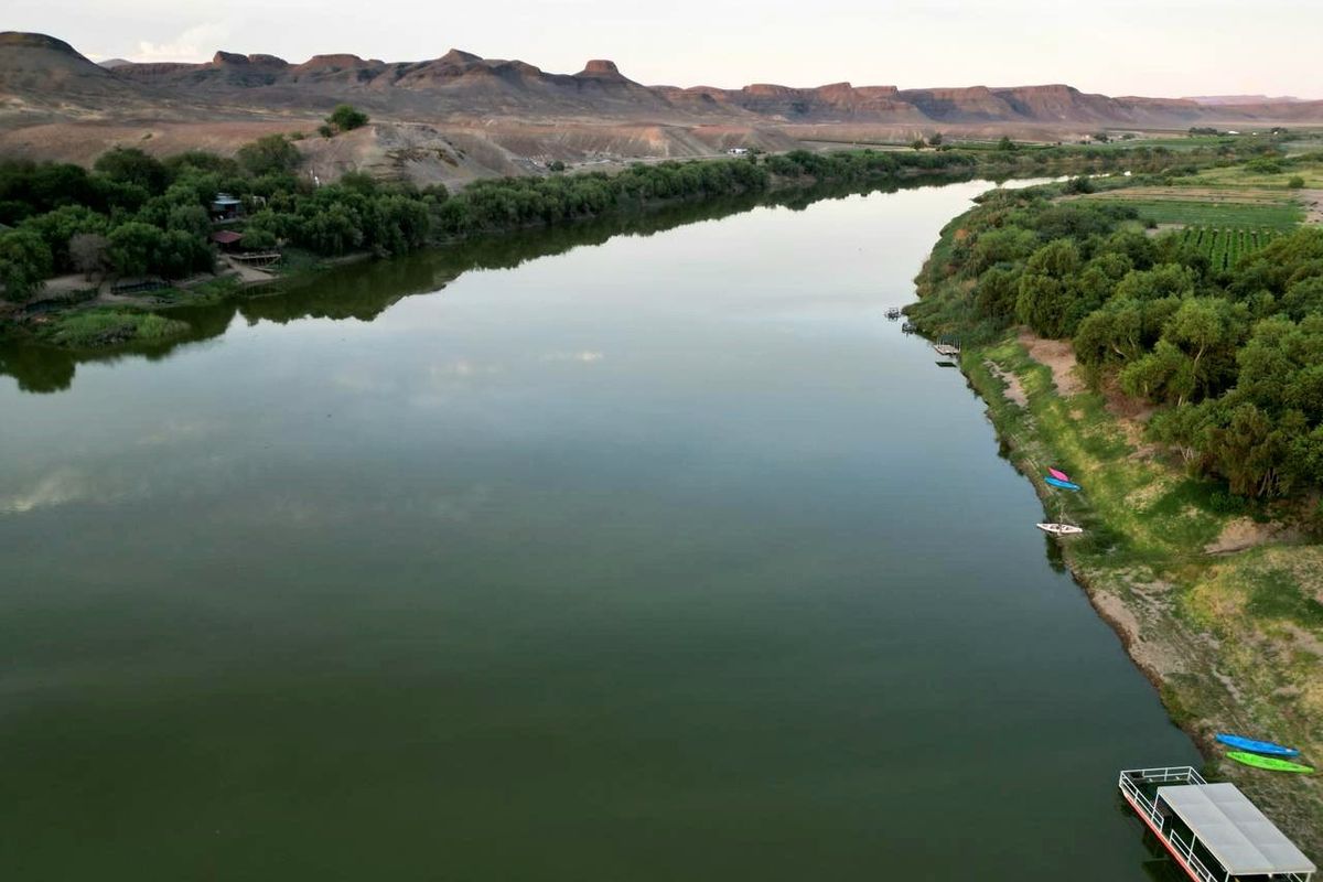 An aerial view of a wide river flowing through a scenic landscape with mountains in the background and lush greenery along the banks.