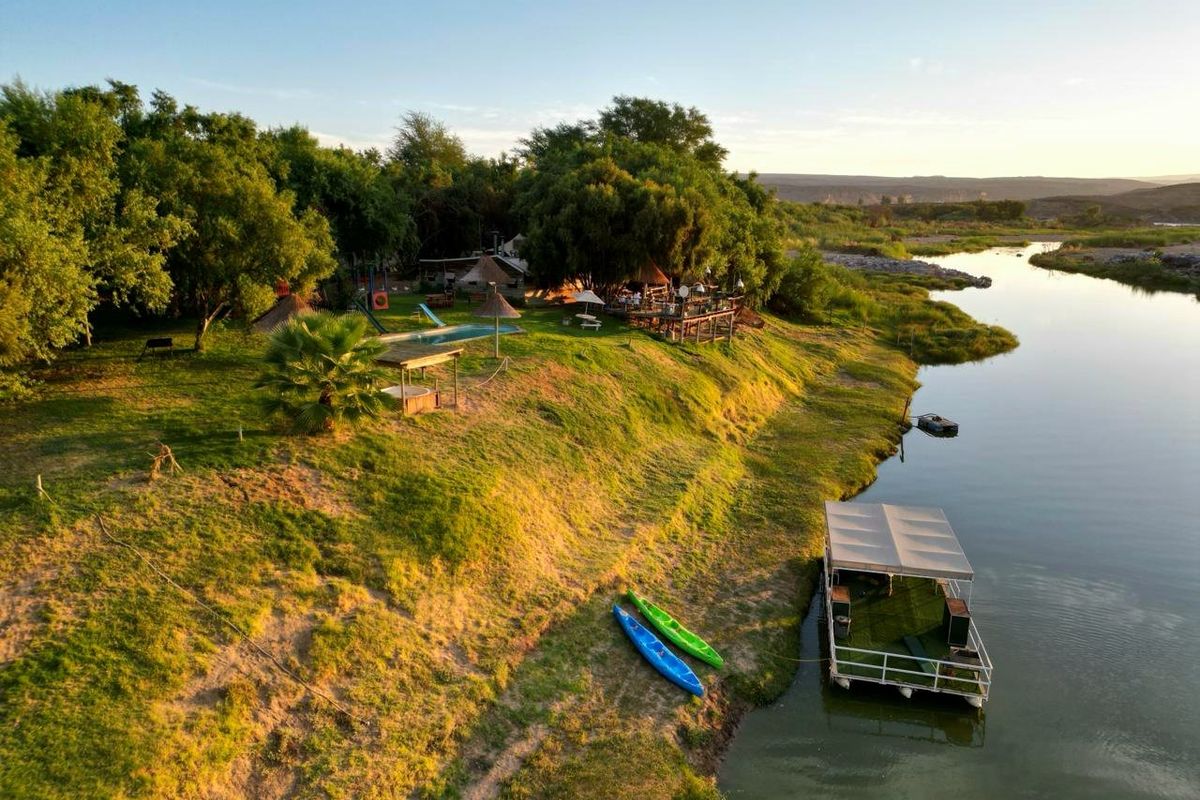 Aerial view of a riverside commercial property featuring a swimming pool, landscaped grounds, and a private floating jetty on the riverbank.