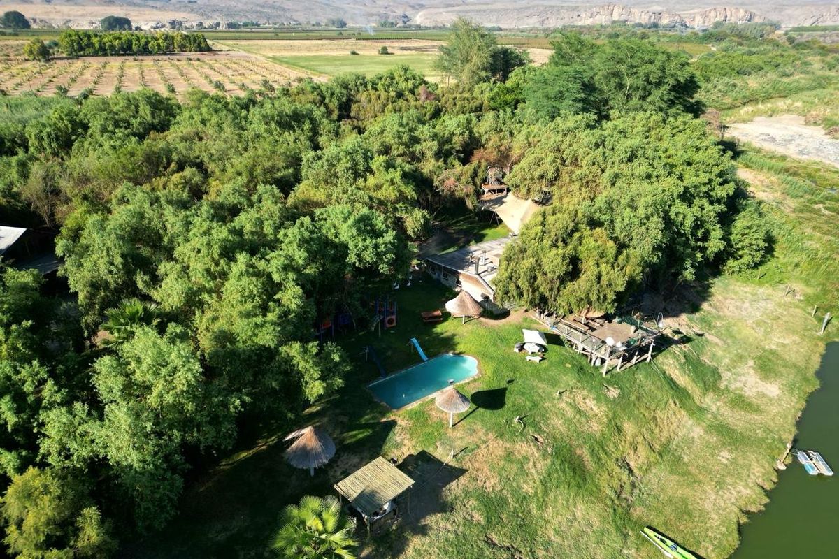 Aerial view of a riverside property featuring a swimming pool, thatched umbrellas, and lush garden surroundings with scenic mountain views.