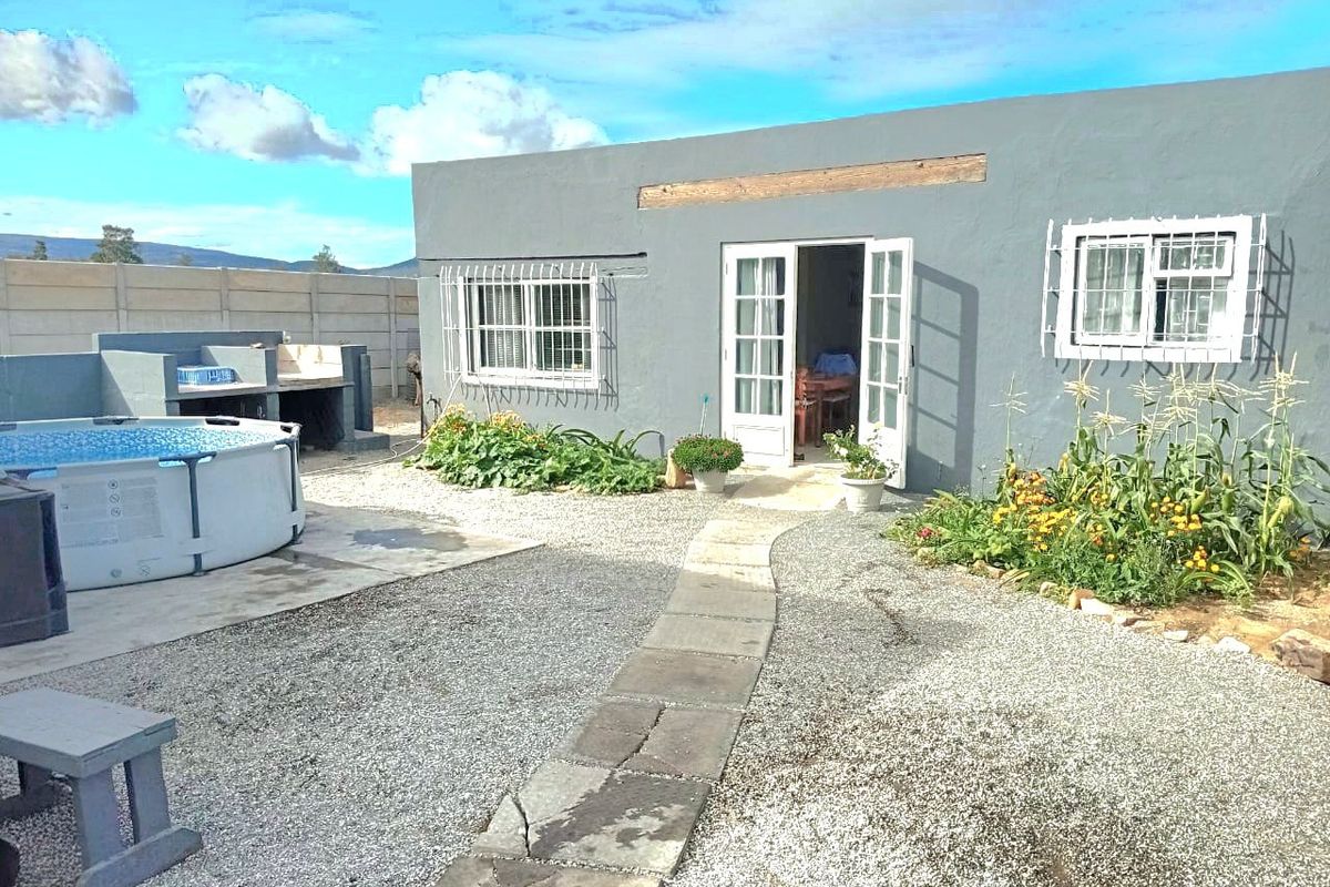 Rear exterior view featuring a gravel garden, paved walkway, built-in braai area, and french door access to the main dwelling.