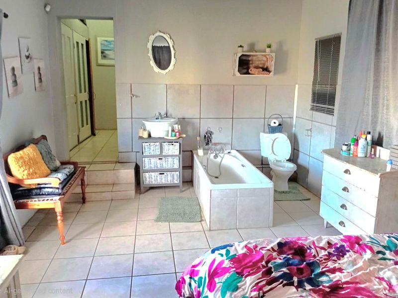 A bathroom featuring tiled walls and flooring, a built-in bathtub, and a toilet, with an adjacent hallway entrance.