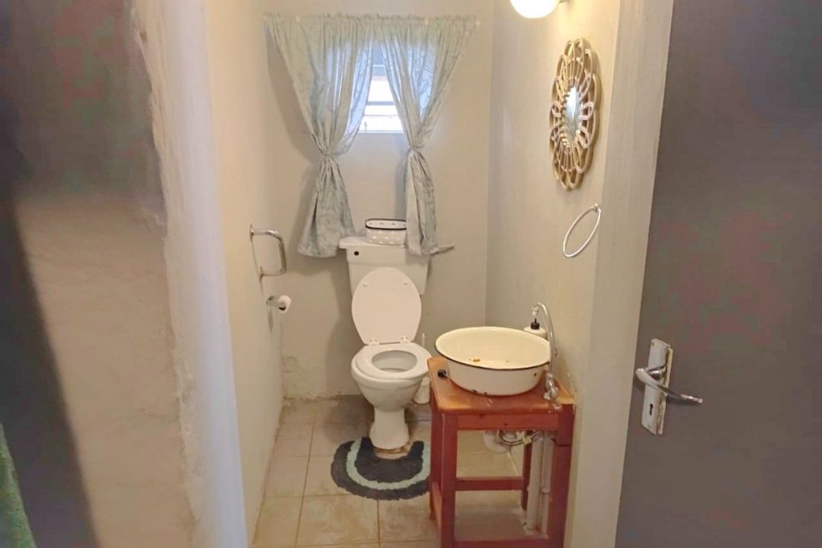 A small, dated bathroom featuring a basic toilet and basin, requiring cosmetic updates and wall repairs to improve its overall condition and appeal.