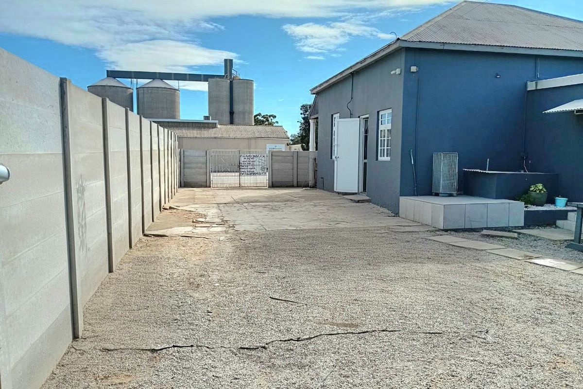 Rear exterior area featuring a gravel driveway, precast concrete boundary walls, and a tiled patio step leading to the main structure.