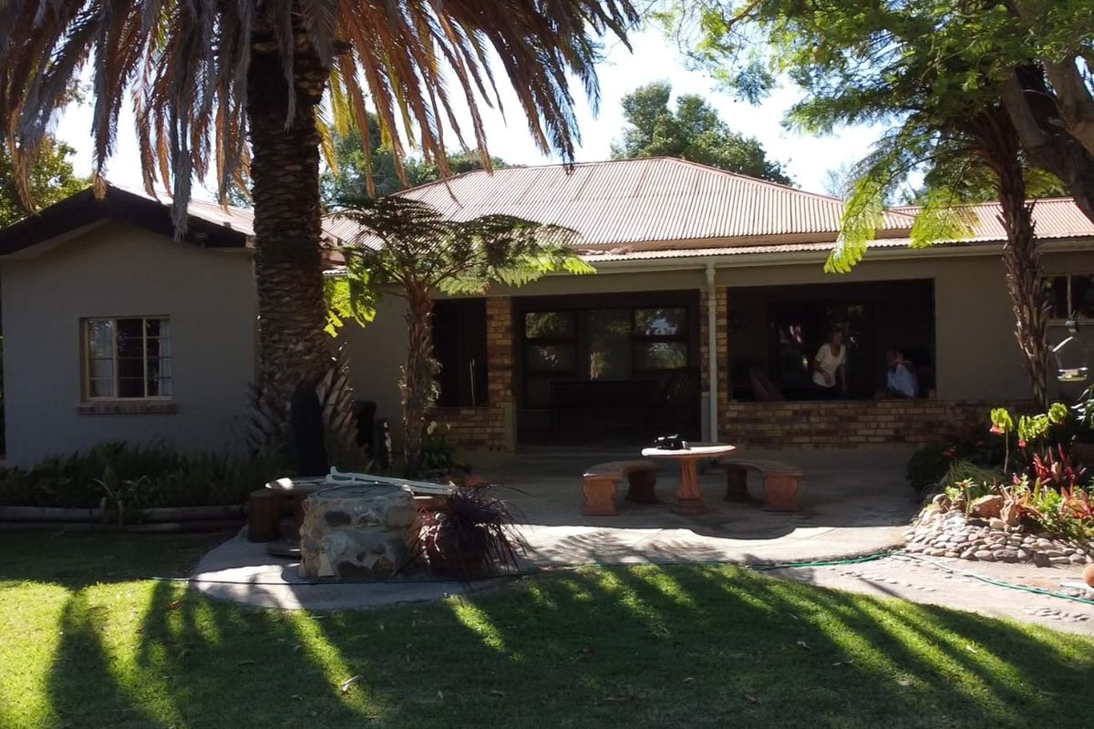 Rear view of the farm property featuring a covered patio area, brick and plaster exterior, and a landscaped garden with mature trees.