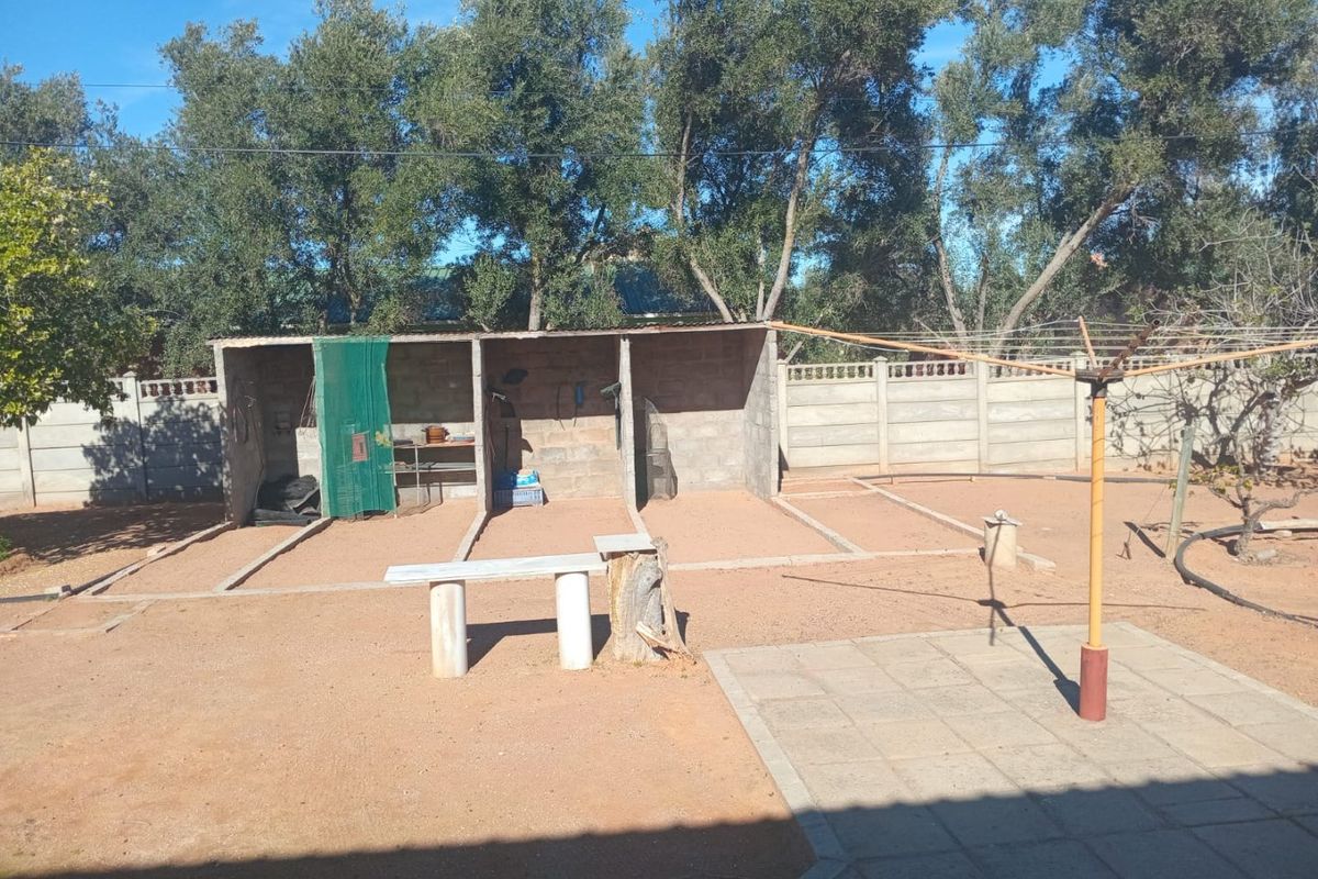Rear garden area featuring a paved patio, rotary clothesline, and three open-fronted concrete storage bays enclosed by a precast boundary wall.