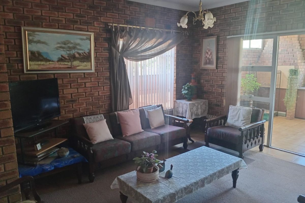 A living room featuring exposed brick walls, carpeted flooring, and a sliding glass door providing access to an outdoor patio area.