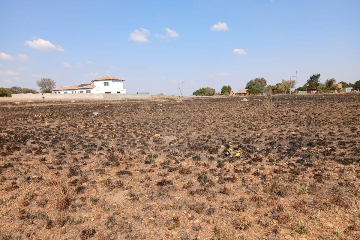 A wide-angle view of a vacant residential plot featuring scorched earth and a distant boundary wall under a clear blue sky.