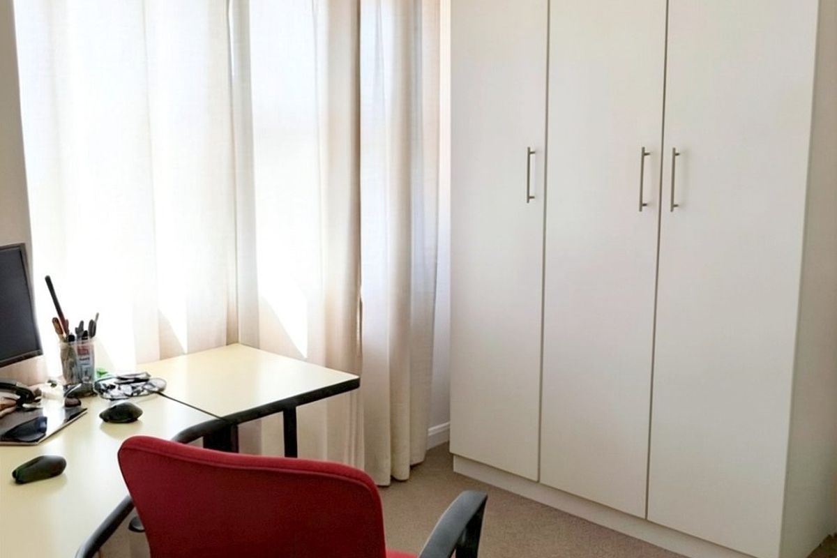 A functional bedroom featuring a built-in wardrobe and neutral carpeting, currently utilized as a home office space.