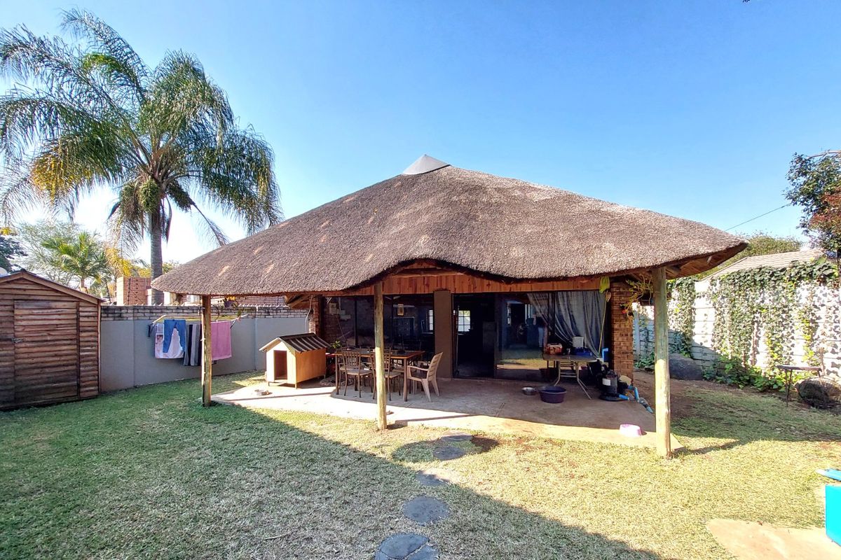 Rear view of the property featuring a covered patio with a traditional thatch roof, sliding glass doors, and a spacious garden area.