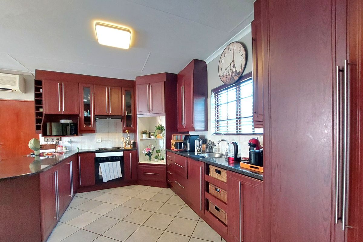 A functional kitchen featuring dark wood cabinetry, granite countertops, integrated oven, extractor fan, and tiled flooring with an adjacent air conditioning unit.
