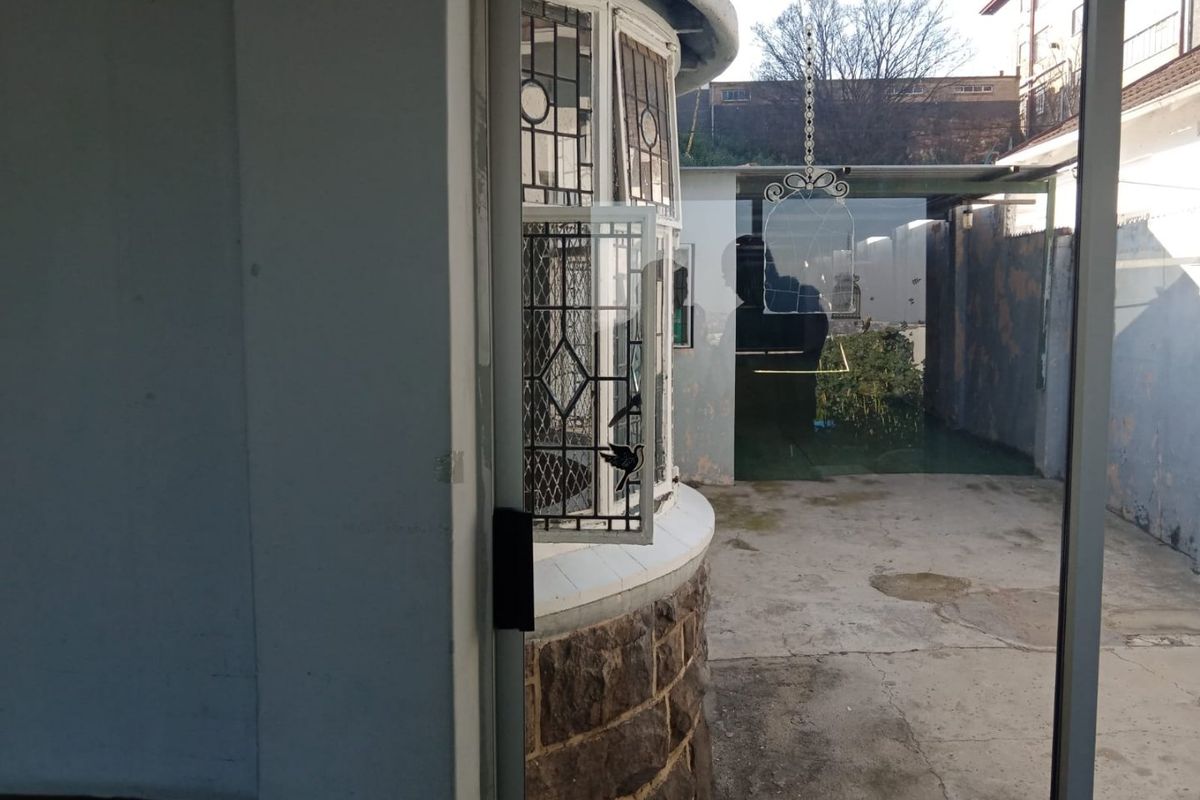 Rear exterior view showing a stone-clad bay window, concrete patio area, and boundary wall with visible signs of weathering and wear.