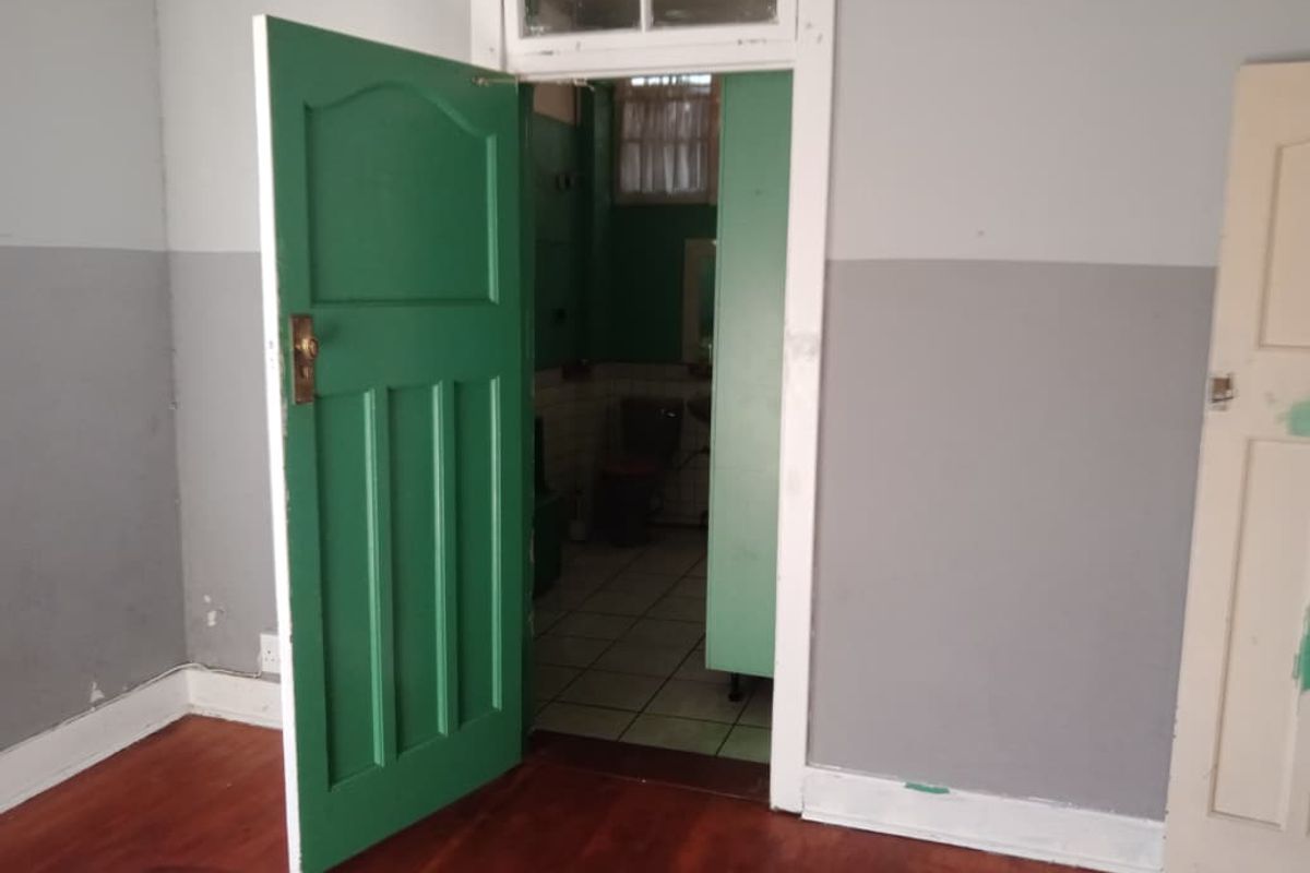A vacant bedroom featuring timber flooring and a green painted door leading into an adjacent bathroom area.