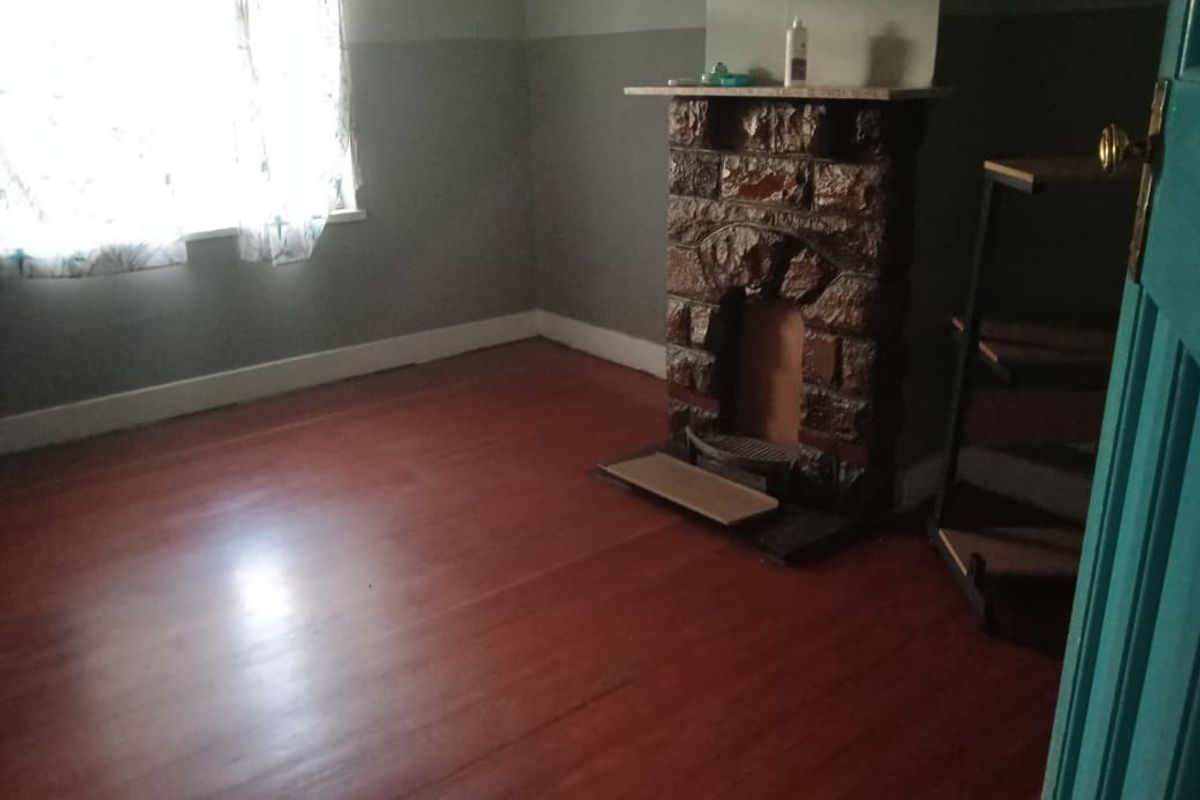 An empty living room featuring original timber flooring and a prominent stone fireplace, offering a blank canvas for renovation and interior design updates.