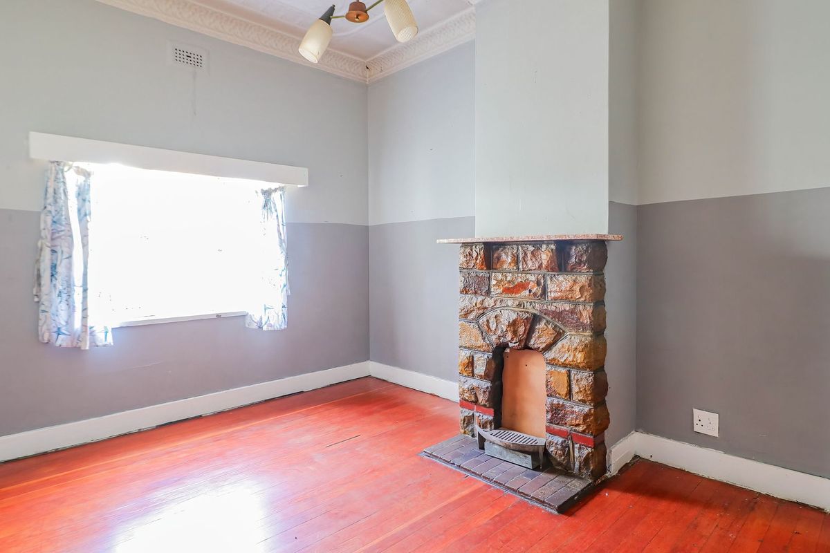 An empty living room featuring original hardwood flooring, a character stone fireplace, and decorative ceiling cornicing.