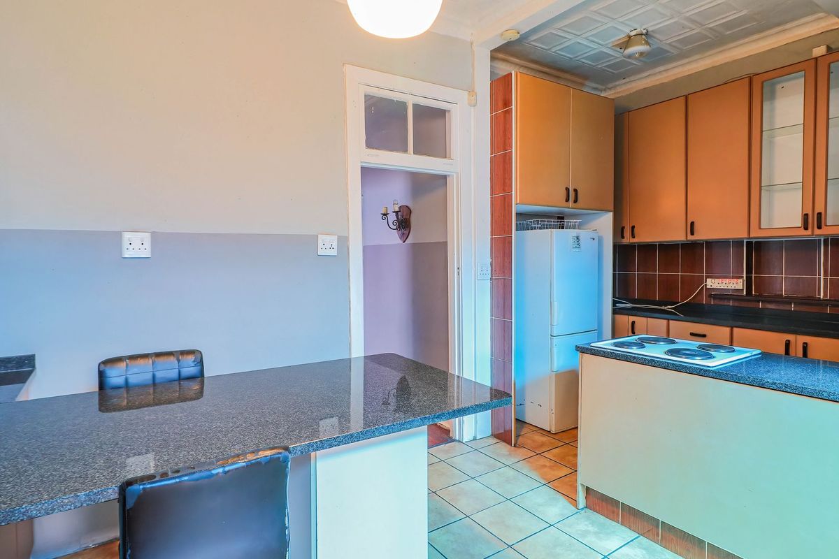 A dated kitchen featuring granite countertops, built-in cabinetry, and an electric hob, offering potential for a modern renovation.