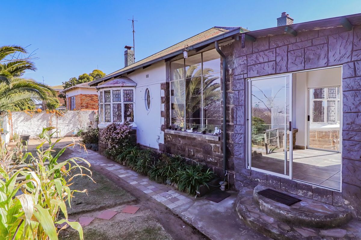 Rear view of the house featuring stone cladding, a bay window, and a sliding glass door leading to a paved patio area.