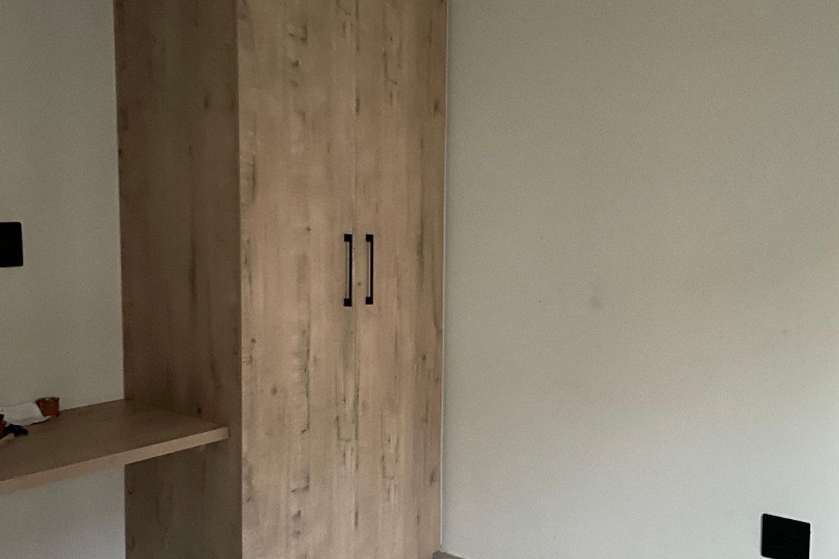A clean, empty bedroom featuring light wood-grain built-in cabinetry, a matching built-in desk, and neutral tiled flooring.