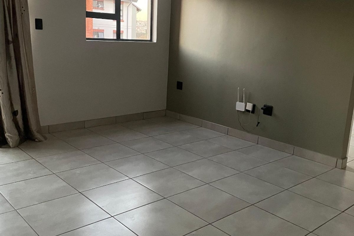 A bright, empty living room featuring neutral tiled flooring, an accent wall, and modern ceiling-mounted spotlighting.