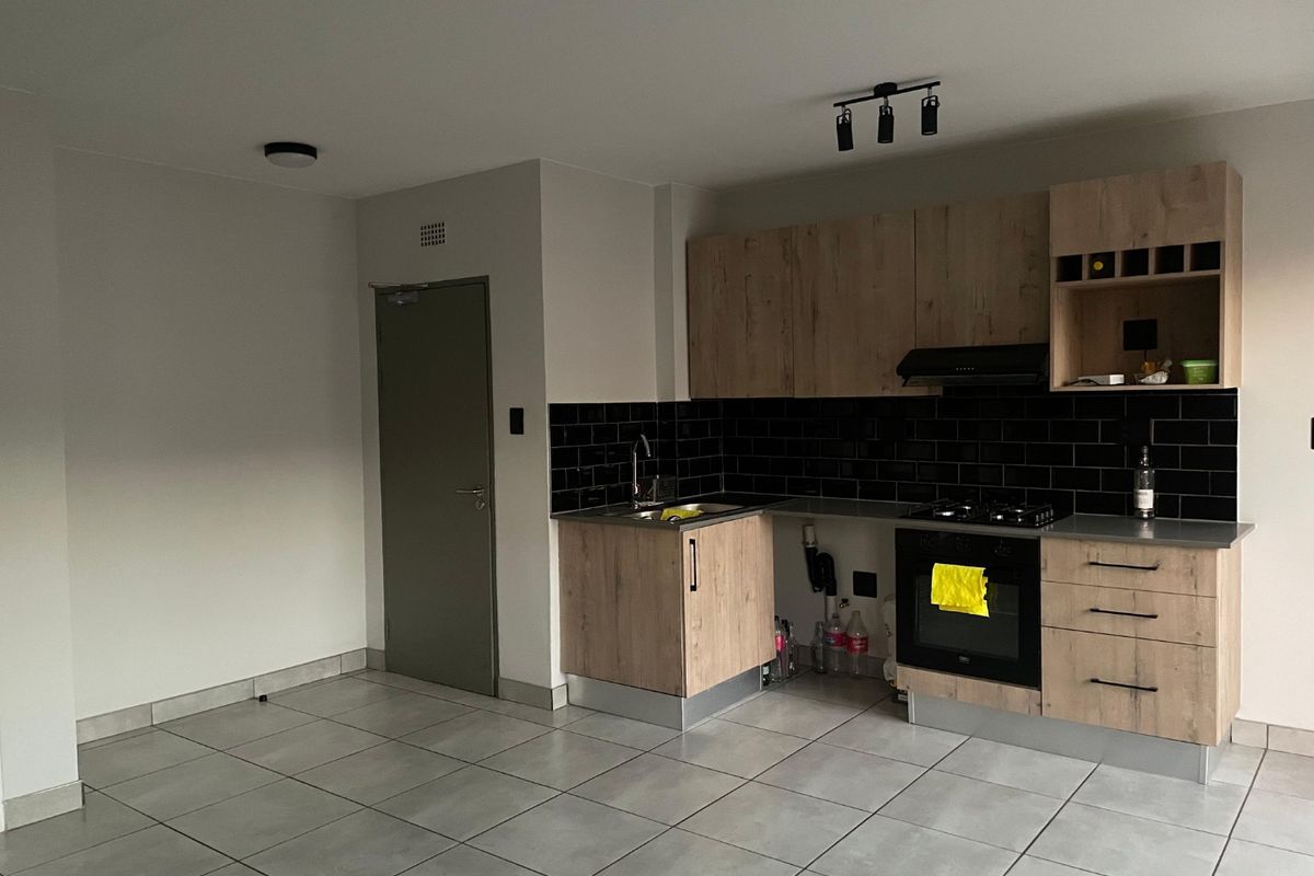 Modern kitchen featuring wood-look cabinetry, black subway tile backsplash, built-in oven, gas hob, and tiled flooring in an open-plan layout.