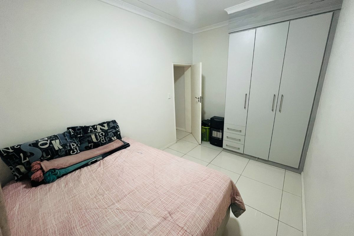 A clean bedroom featuring neutral tiled flooring, white walls, and a modern built-in wardrobe with ample storage space.