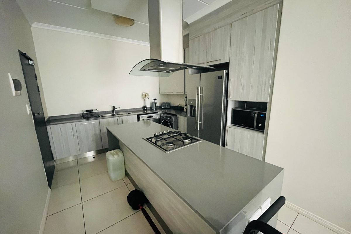 Modern kitchen featuring a central island with a gas hob, overhead extractor fan, ample built-in cabinetry, and tiled flooring.